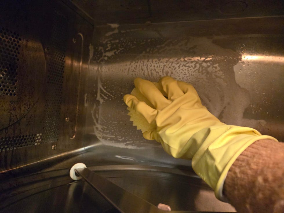 cleaning inside of a microwave with a scrub daddy scrubber and gloves