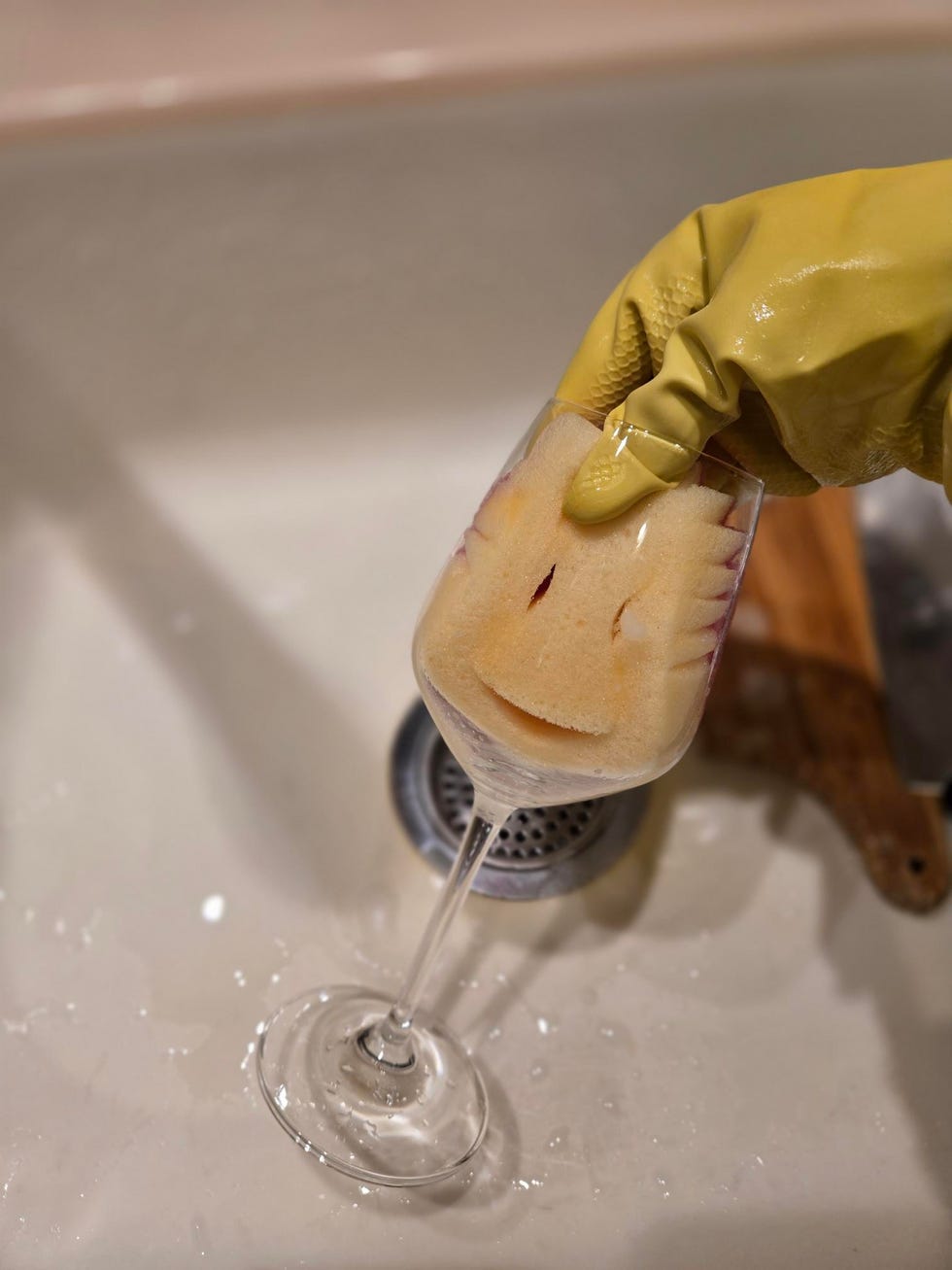 cleaning a wine glass with a scrub mommy sponge while wearing a rubber glove