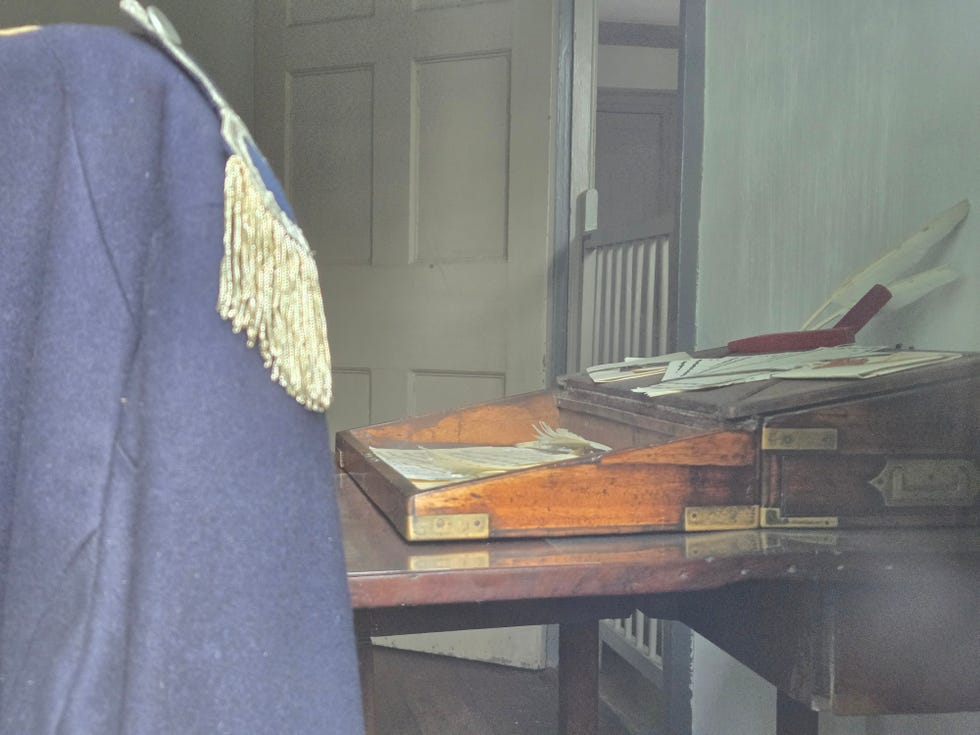 a writing desk and replica officer's jacket in ford mansion, where washington might have penned his response to ﻿condict’s letter that precautions had been taken against invasion.﻿