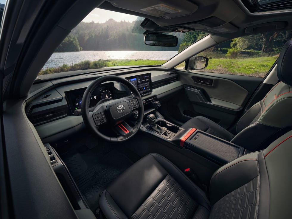 interior view of a vehicle cabin featuring a digital dashboard, central touchscreen, and two tone seats with red accents.