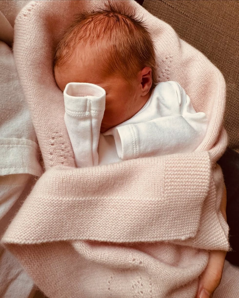 An infant wrapped in a soft pink blanket, held gently