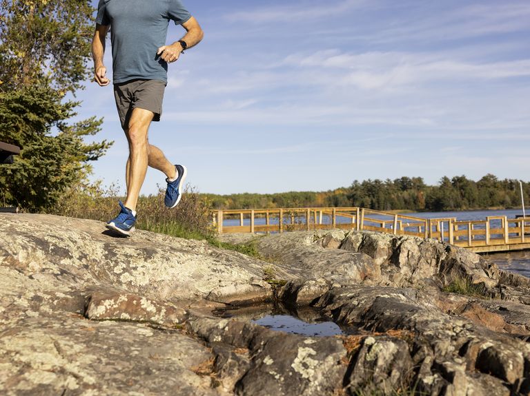 man running on rocks in front of dock on water