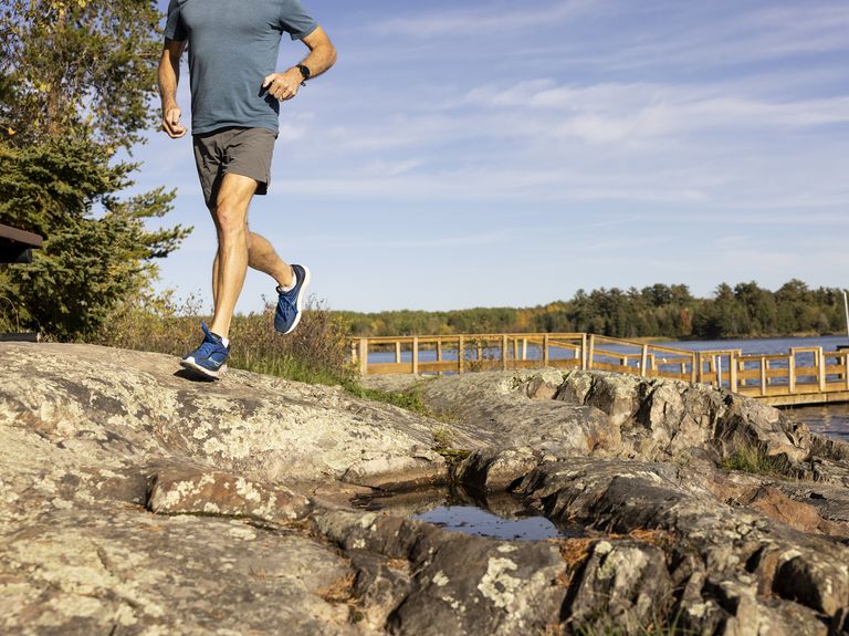 man running on rocks in front of dock on water