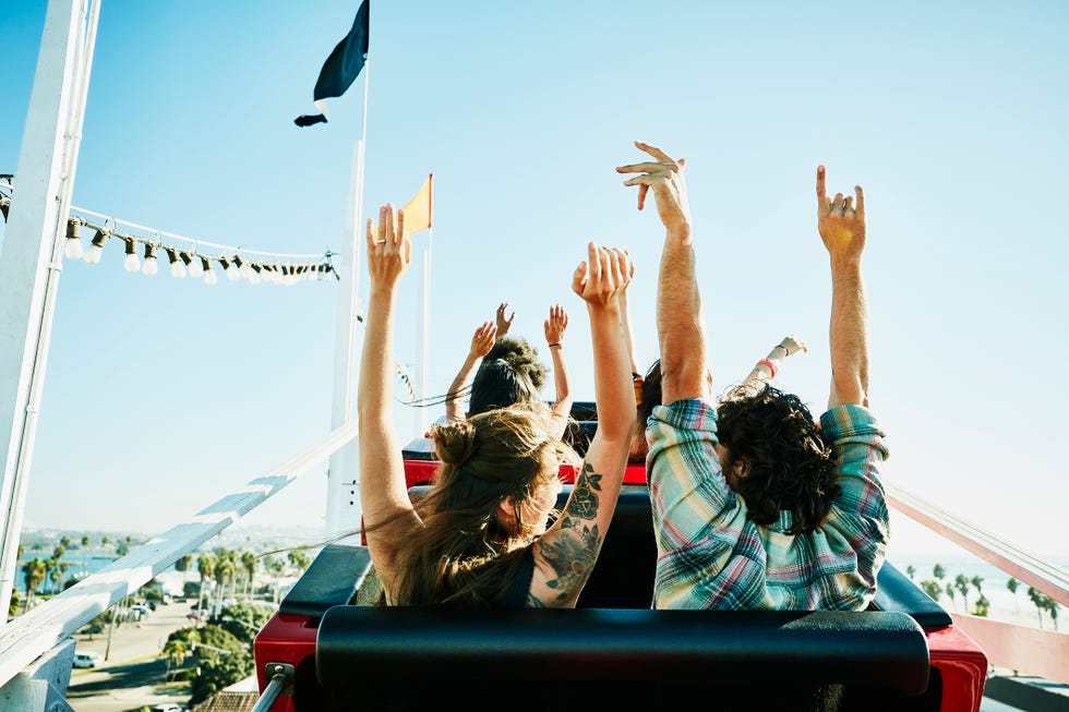 rear view of couple with arms raised about to begin descent on roller coaster in amusement park