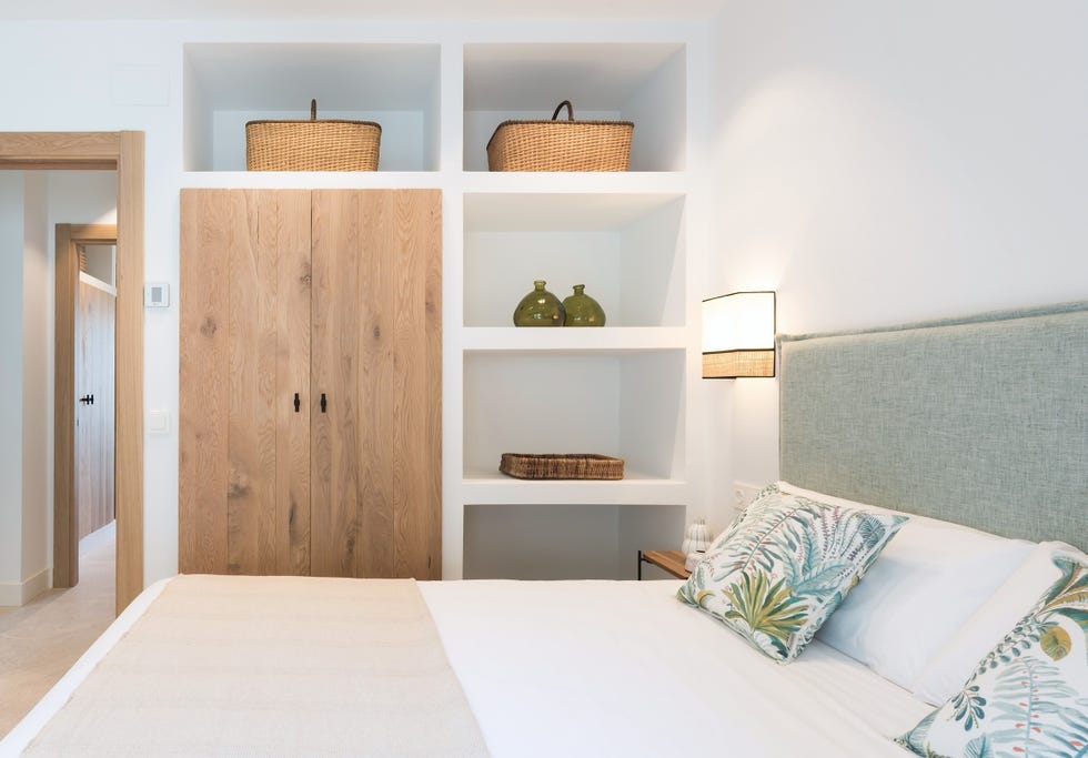 cama con cabecero tapizado en verde y estantería de obra con puertas de madera