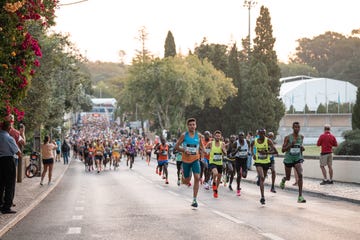 a group of people running on a road with trees and buildings in the background