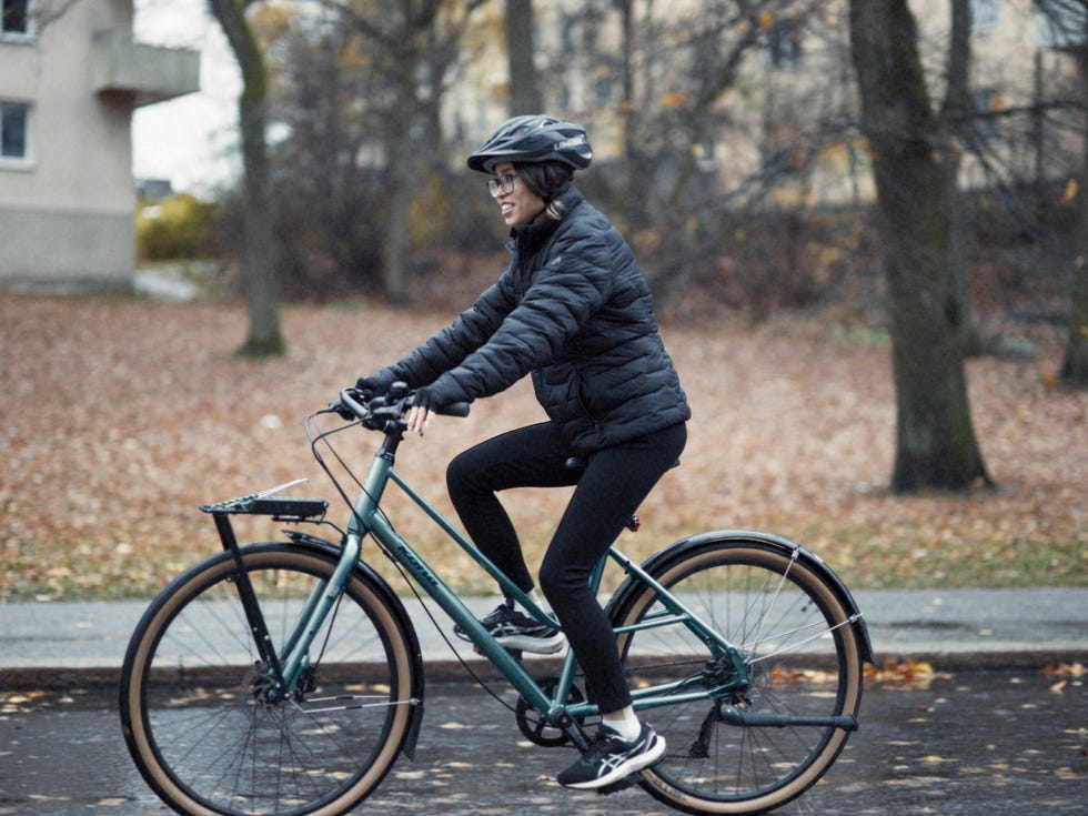 a cyclist wearing a helmet and a black jacket pedaling a bicycle along a pathway surrounded by fallen leaves