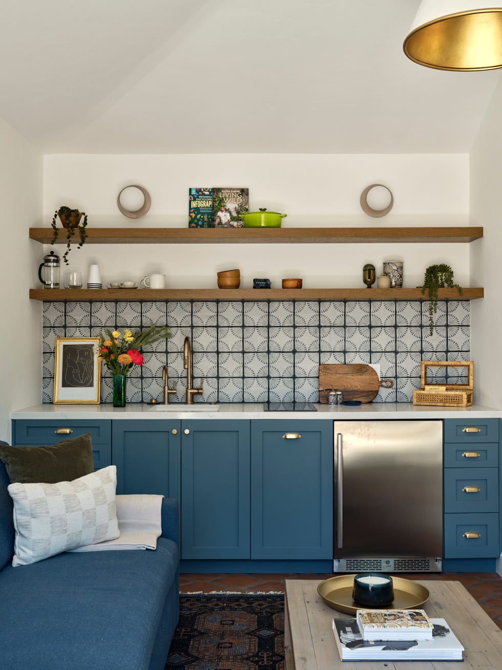 a small kitchen features blue cabinetry with golden handles, complemented by a minimalist countertop and a sleek stainless steel refrigerator