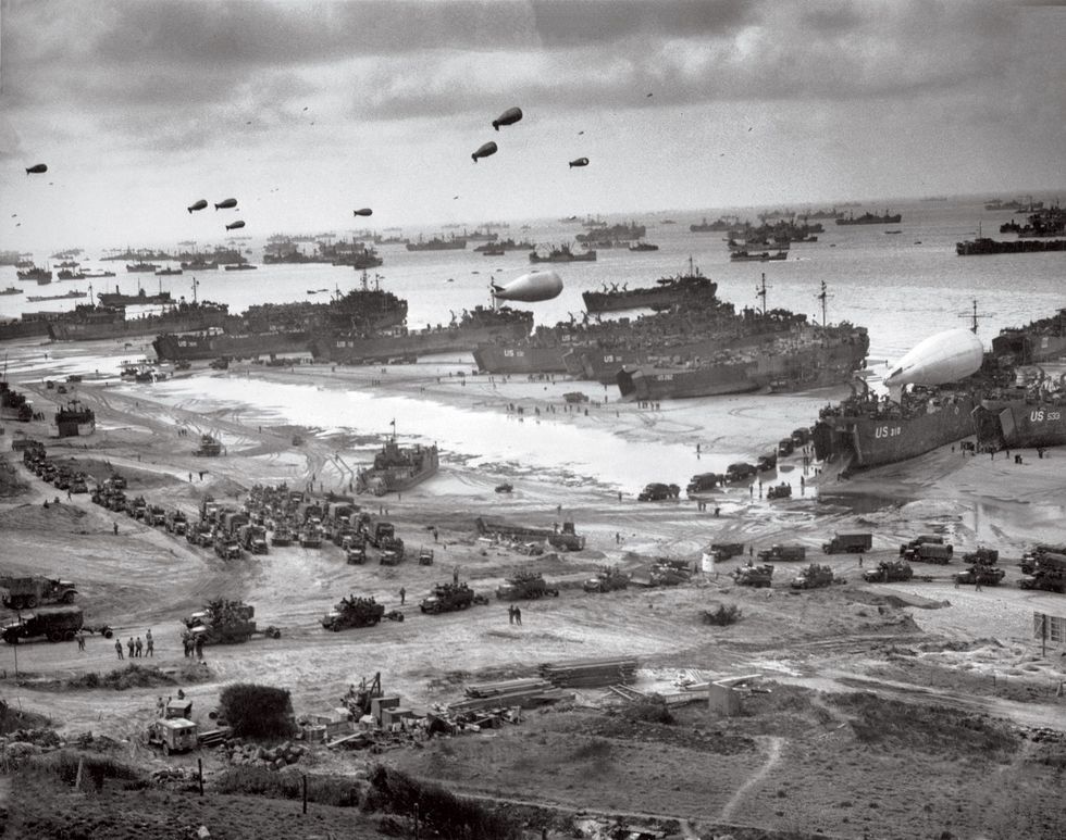 Op 8 juni 1944 worden tanks en trucks vanuit landingsvaartuigen afgezet op Omaha Beach dat onder sperballonnen ligt Met de zware metalen kabels waarmee de ballonnen waren verankerd werden laagvliegende jachtbommenwerpers op afstand gehouden