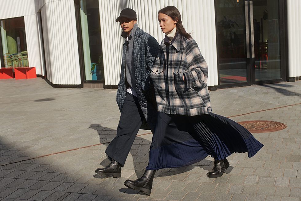 two models wear oversized, long coats with black shoes on an outside patio, as part of claire waight kellers first collaboration with uniqlo