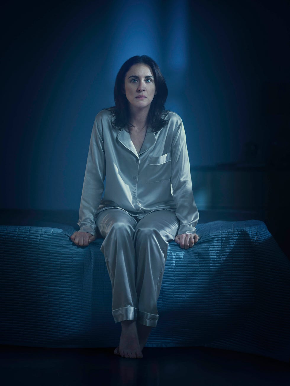 a person sitting on a bed in a dimly lit room with a smooth fabric quilt