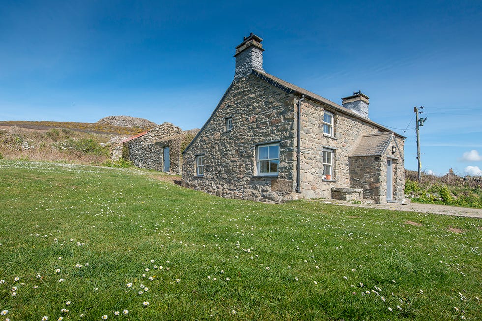 a cobbled cottage sits in the countryside surrounded by grass and blue sky
