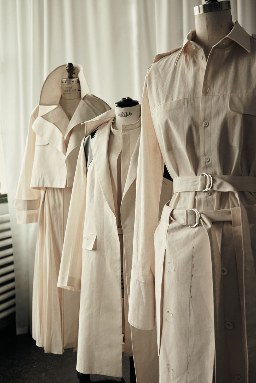 three trench coats with different collars on mannequins in a design studio, from an upcoming collaboration between peter do and banana republic