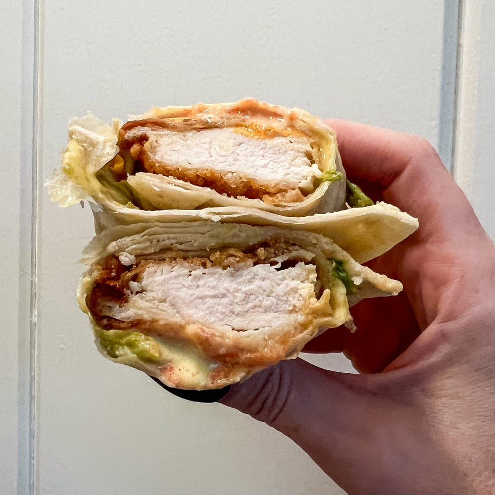 a hand holding a cut wrap sandwich revealing layers of chicken sauce and lettuce