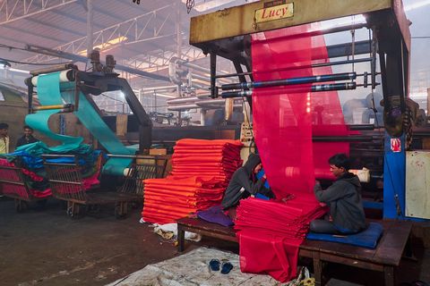 Textielarbeiders in de Saree Factory halen banen chiffon uit reusachtige weefmachines De stoffen worden geproduceerd in banen met een lengte van soms wel vijfhonderd meter en dan in kortere saridoeken gesneden