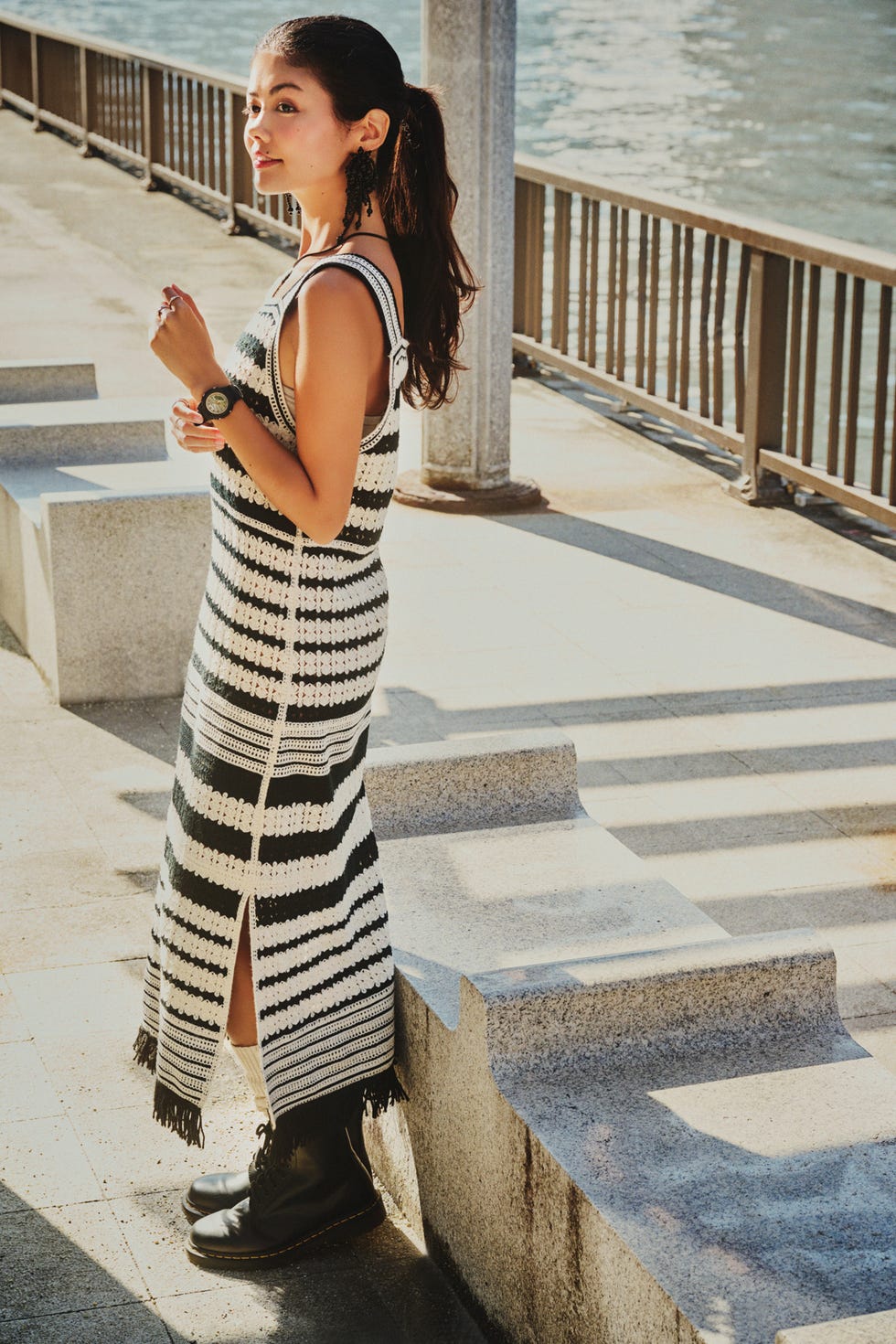 a woman in a dress standing on a stone walkway by the water