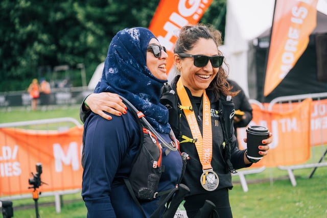 Two women celebrating after a race one holding a coffee and the other wearing a medal