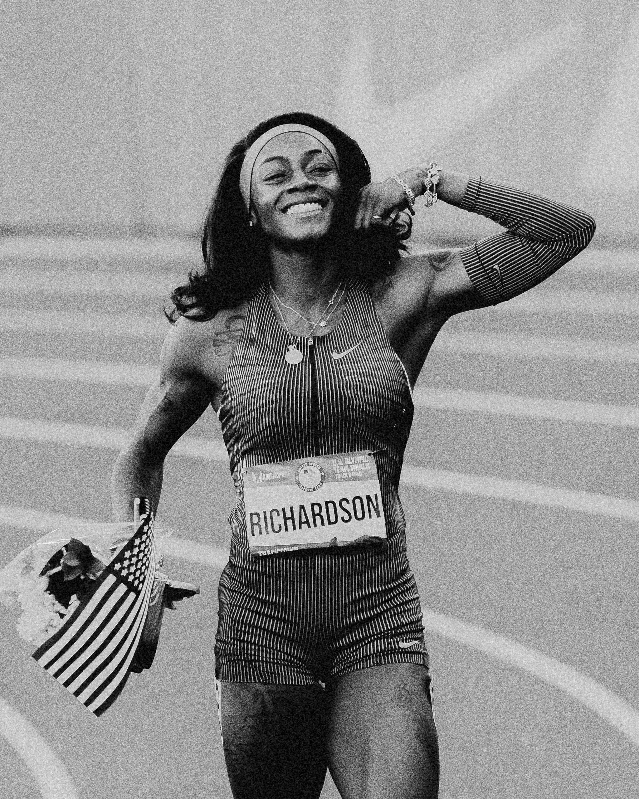 a woman track athlete celebrates while holding an american flag and flowers