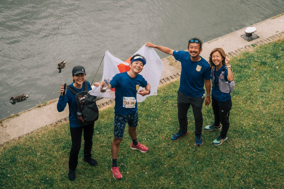 four people standing and smiling while holding a japanese flag