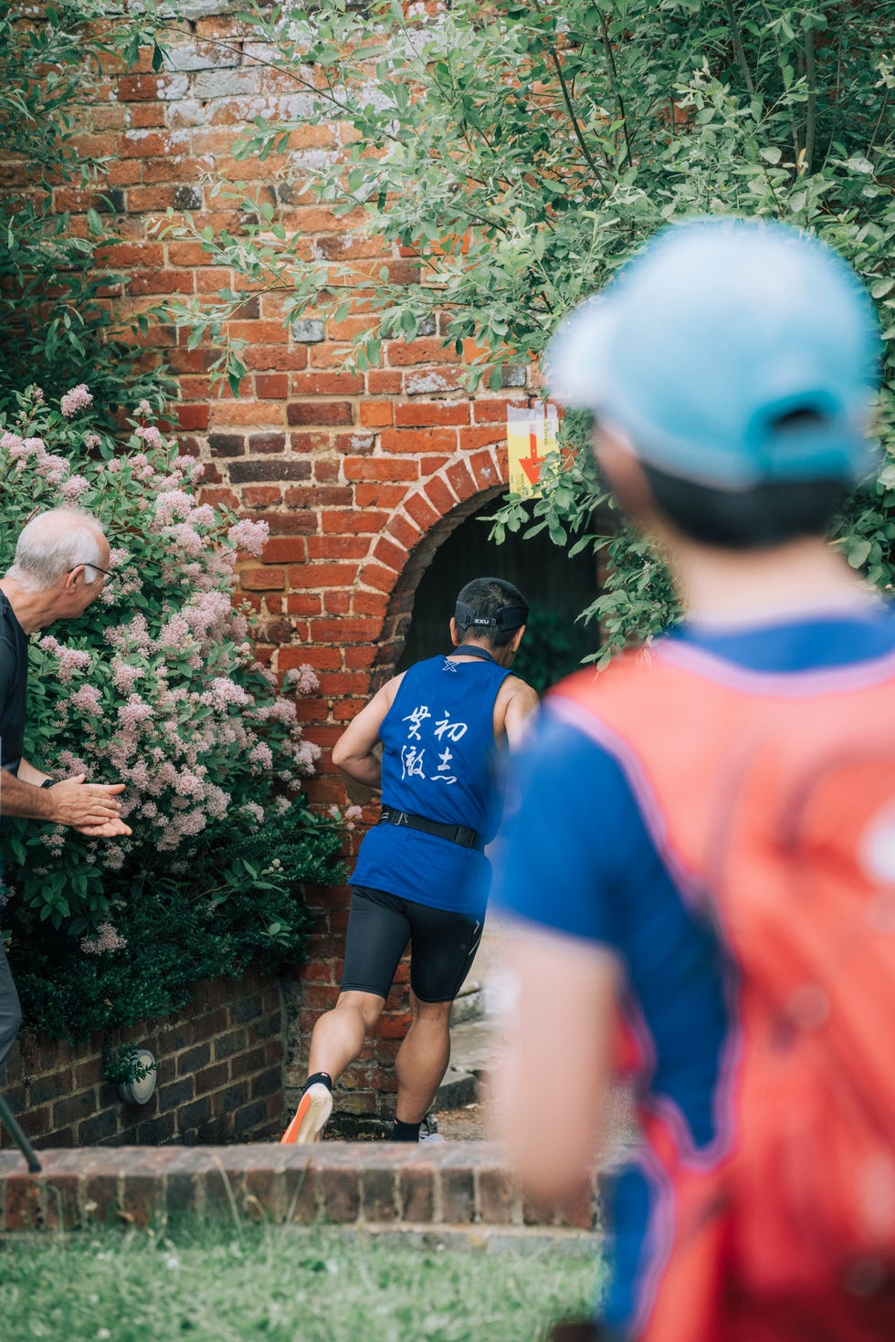 runner approaching a brick archway surrounded by greenery and flowers