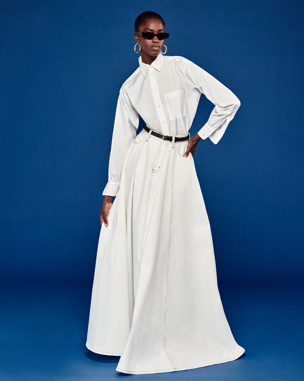 model wearing a long white shirt and a flowing white skirt against a blue background