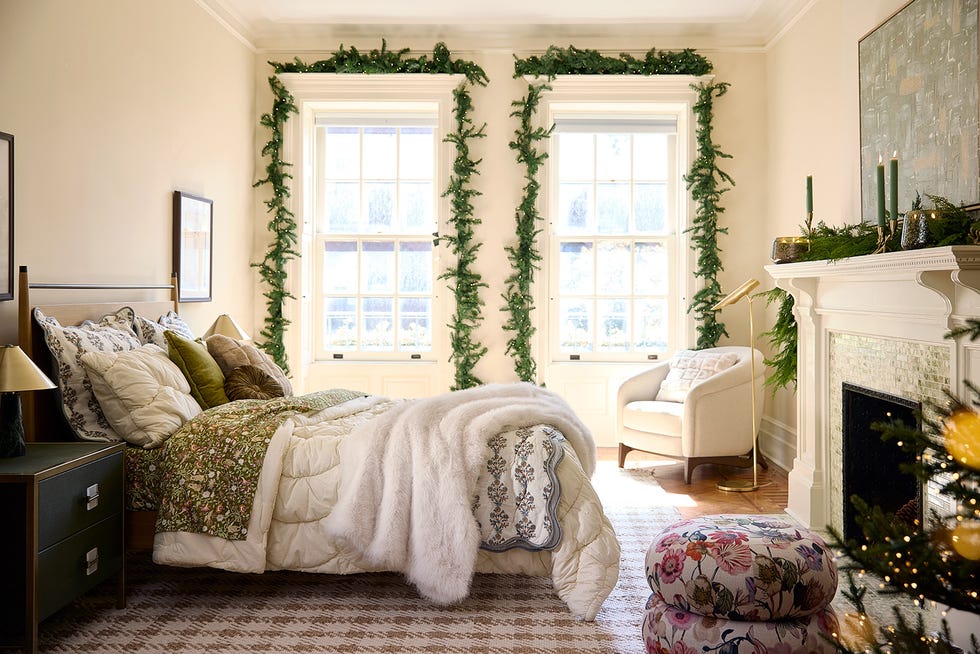 bed with plush white and grey and sage green bedding, next to windows draped in green christmas garlands