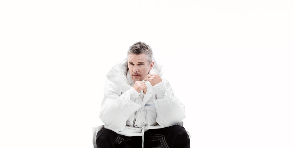 ethan hawke seated in a comfy pose wearing a large white jacket