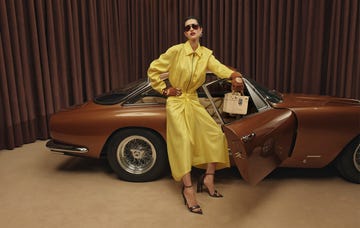 woman in a yellow dress and sunglasses standing in front of a red sports car with an open passenger side door