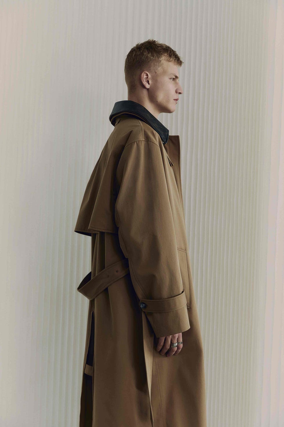 a person wearing a brown coat with a black collar standing in profile