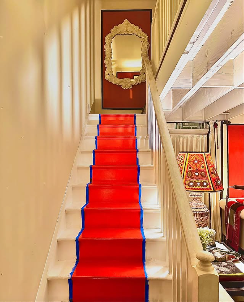 Staircase featuring a red runner and blue tape, leading to a hallway with a decorative mirror.