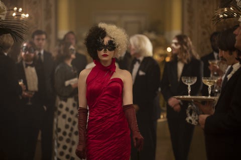 emma stone as cruella de vil at a party with half black, half white wig, red dress and gloves, red lips and feathered mask