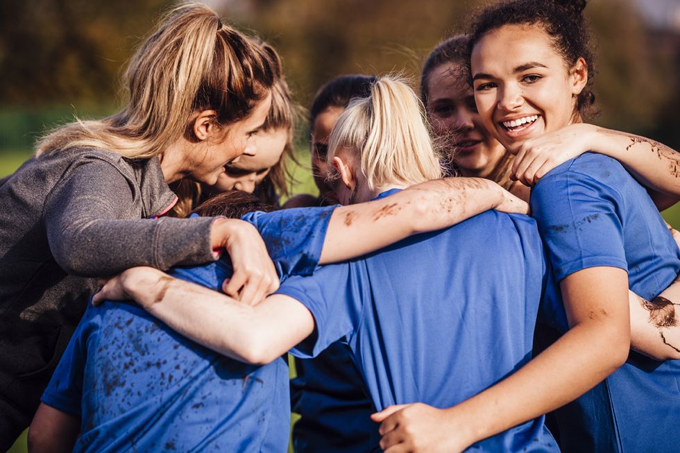 young teenage girls smiles as she gathers around with her team mates for a chat during their rugby game