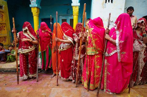Tijdens het Holifeest in de Indiase deelstaat Uttar Pradesh dragen vrouwen de traditionele rode sari en hebben ze bamboestokken bij zich die ze van oudsher gebruiken om de mannen van het dorp een ceremonieel tikje te geven als symbool van de liefde tussen de hindoegoden Krishna en Radha