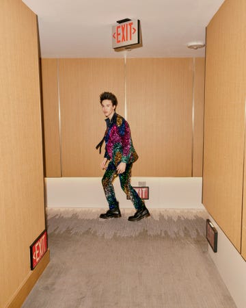 individual wearing a colorful sequined outfit walking in a hallway with exit signs