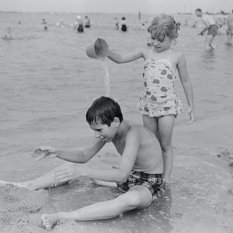 sister pouring water from bucket at his brother  on beach