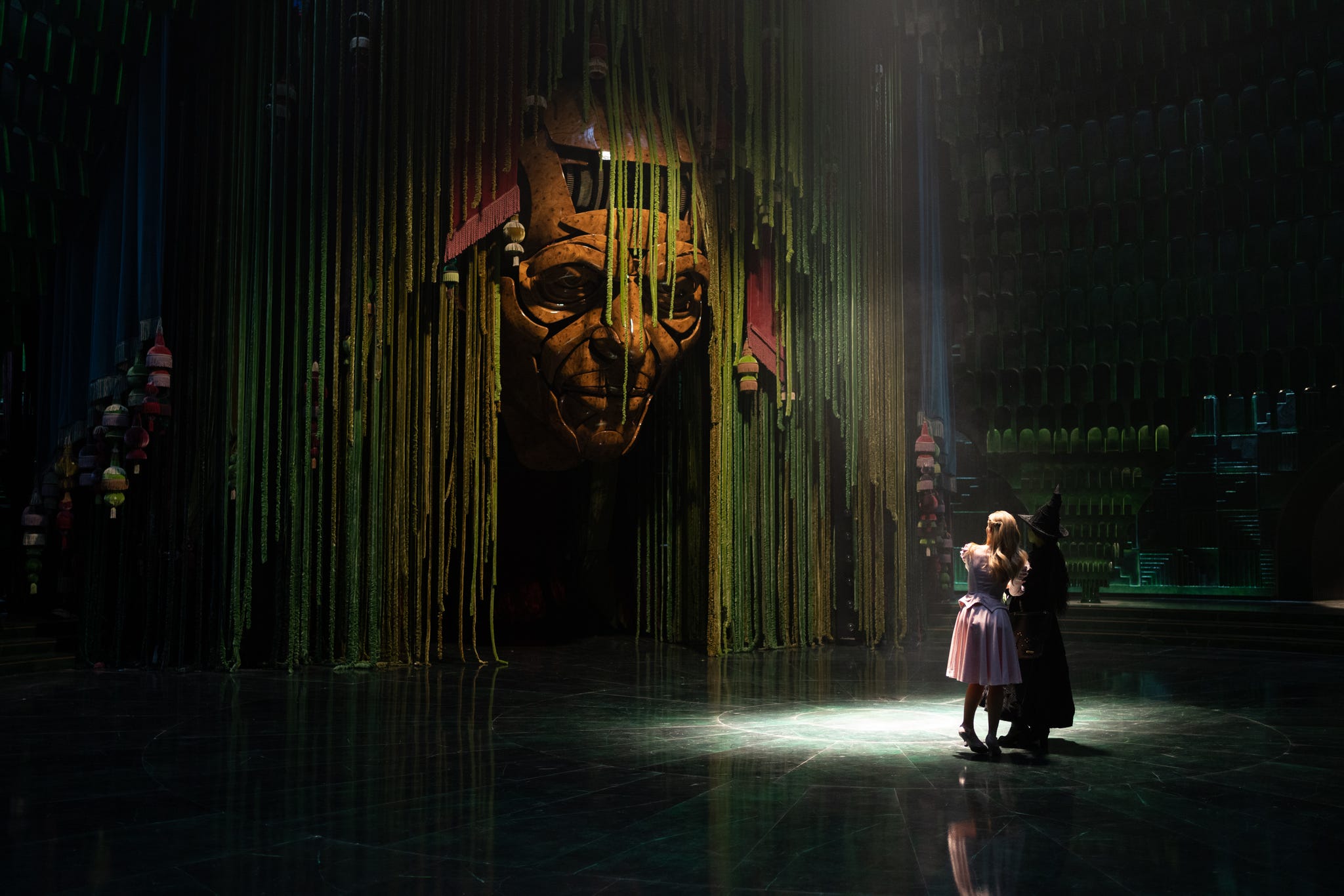 a dramatic stage scene featuring a large mask and two characters