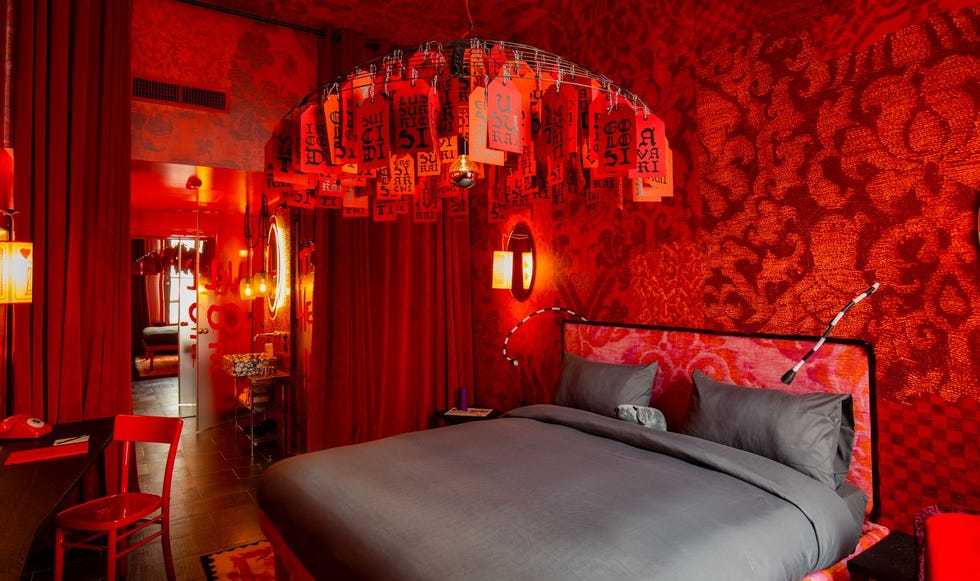 25hours hotel piazza san paolino room interior with a red theme, including upholstered headboard, red chair, chandelier with red tags, and other bold touches