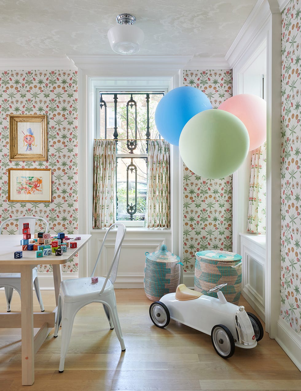 summer thornton’s personal chicago residence designed by summer thornton play room features pink and green floral wallpaper that matches the same patterned drapes, a maple wooden craft table and a fonrasetti wall covering on the ceiling