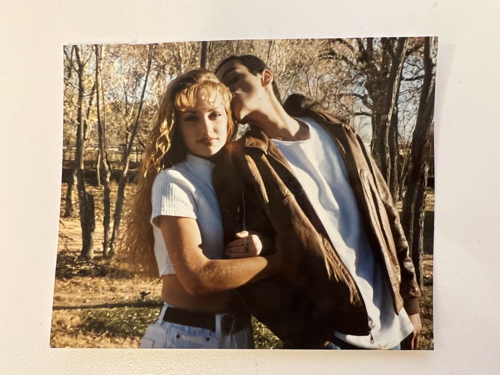actress minka kelly, in a 90s photo, with crispy blond bangs and brown lipstick, poses with her brother, who is kissing her head