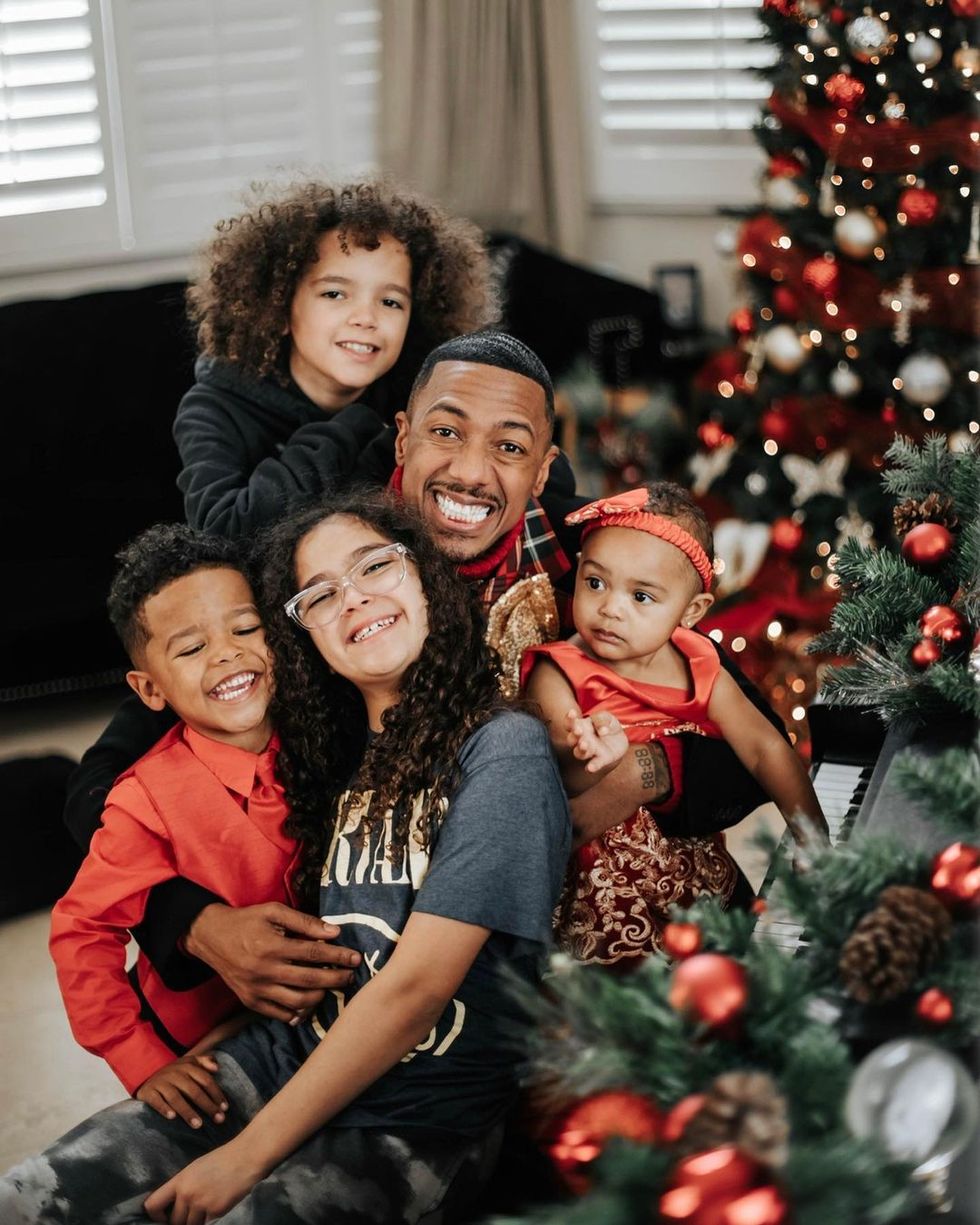 a group of people posing for a photo in front of a christmas tree, nick cannon and his children