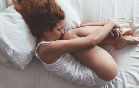 woman curled up on bed with period cramps