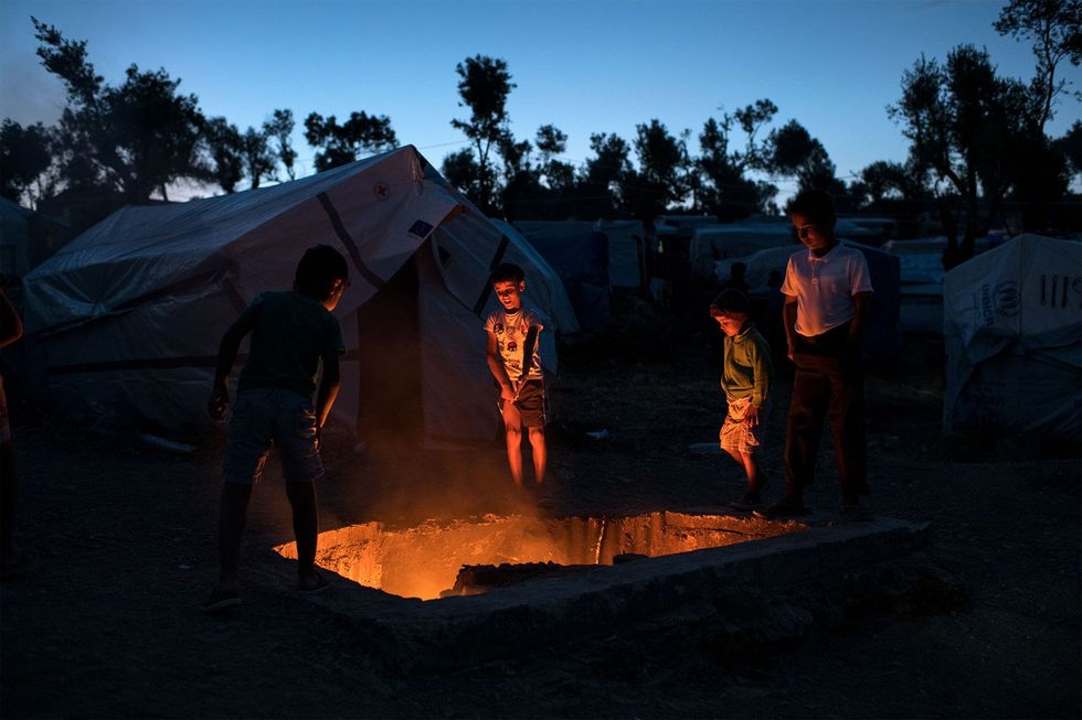 Vluchtelingenkinderen staan rond een kuil met brandend afval Het vuur wordt gebruikt om muggen en insecten op afstand te houden maar veroorzaakt ook rook met giftige chemicalin