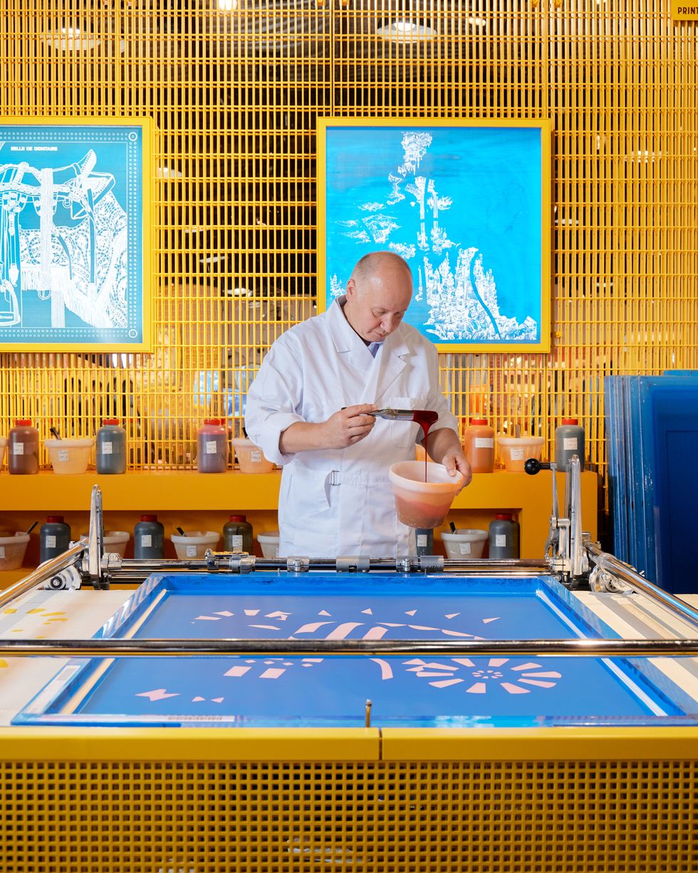 an hermes worker pours dye onto a screen to print a silk scarf