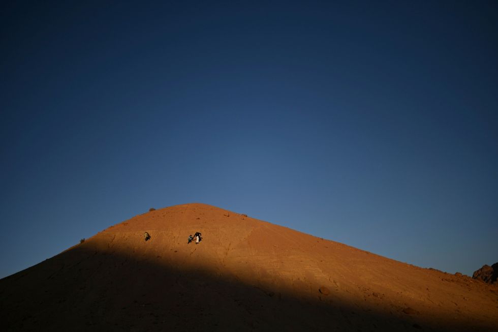In het laatste licht van de zonsondergang loopt een vader met zijn zoon een heuvel op Binnen de bedoeense gemeenschap zorgen vaders voor de kinderen wanneer de moeders soms de hele dag in de bergen zijn om de dorpskudde te hoeden