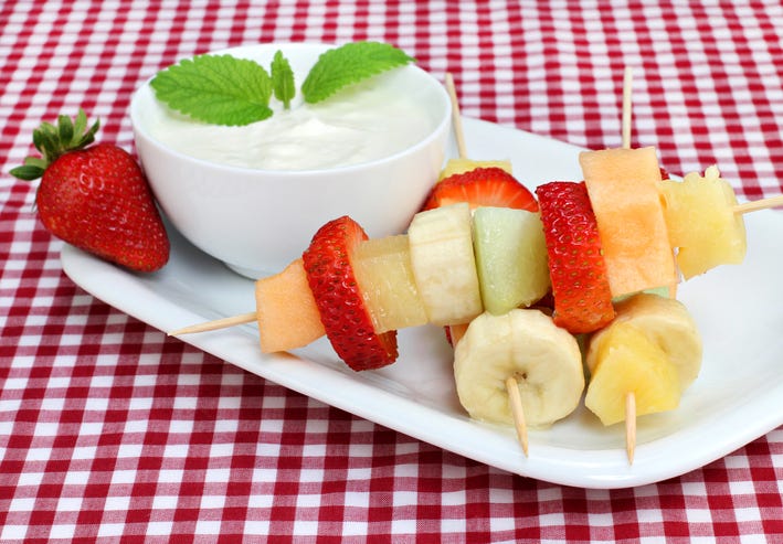 three healthy fresh fruit kabobs with a side of greek yogurt dip, a healthy sweet snack