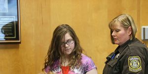 a police officer holding onto the arm of slender man stabbing suspect anissa weier during a courtroom appearance