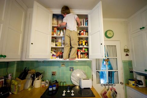 Een jongen klimt op een keukenkastje in zijn huis in Lincoln Nebraska De rijk gevulde kast herinnert aan de wereldwijde verschillen in voedingszekerheid