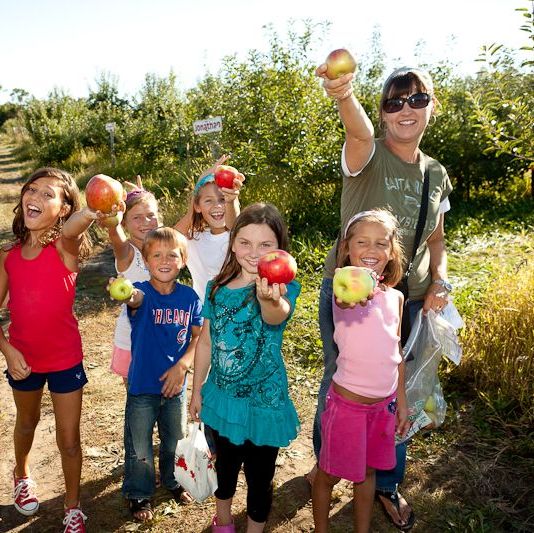 large group of kids and two women in apple orchard holding apples toward camera