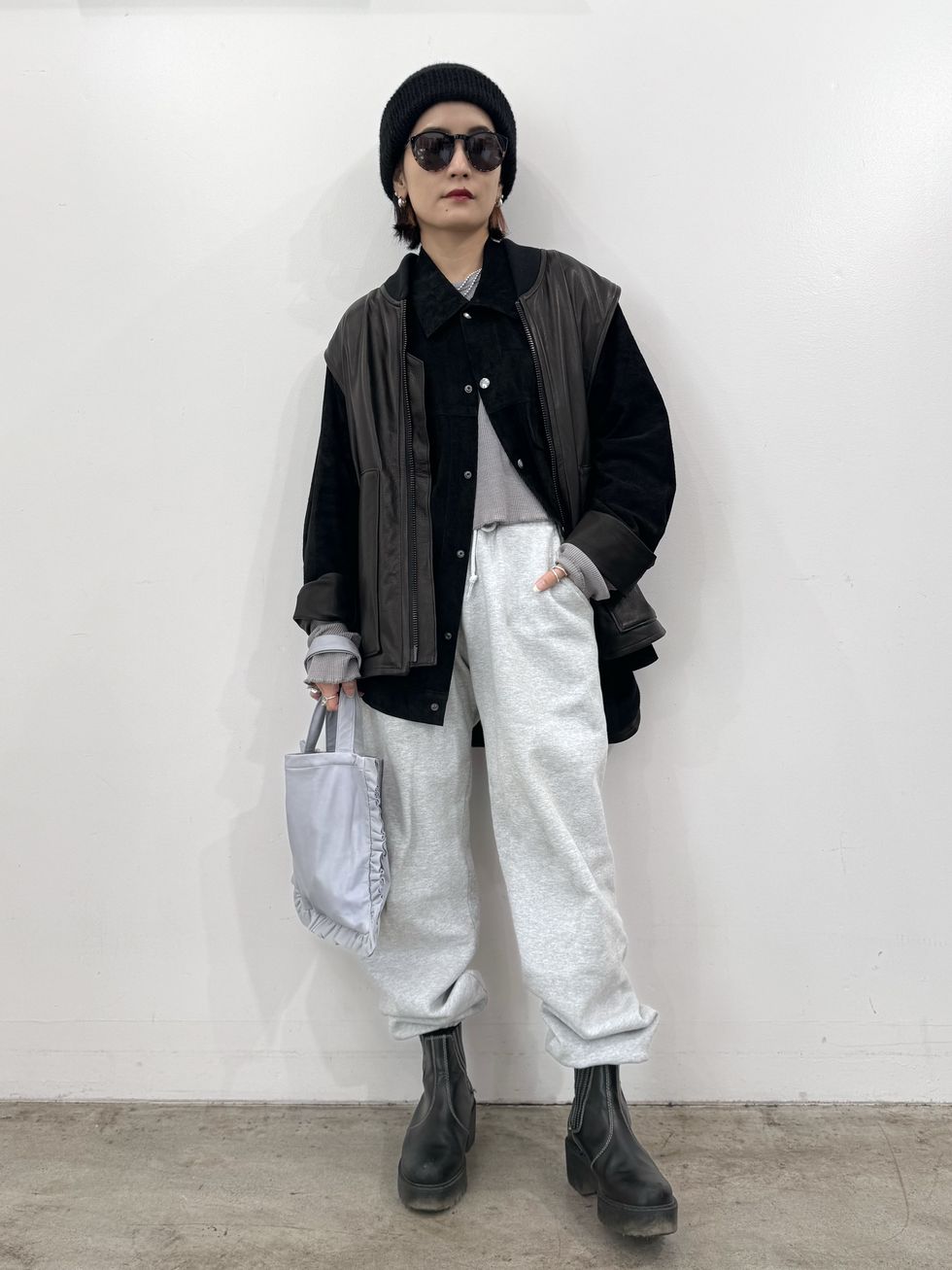 a person wearing a black jacket and white pants holding a white bag
