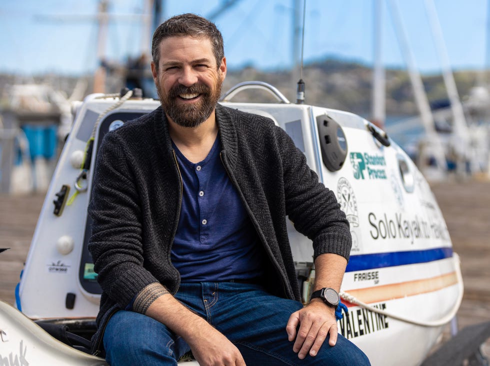 individual seated on a kayak at a dock with sailing boats in the background